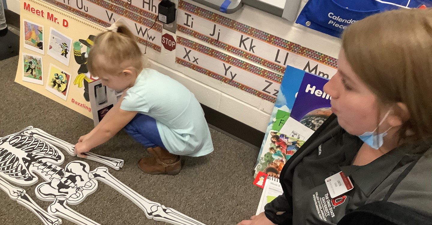 Preschool student works on project while teacher observes