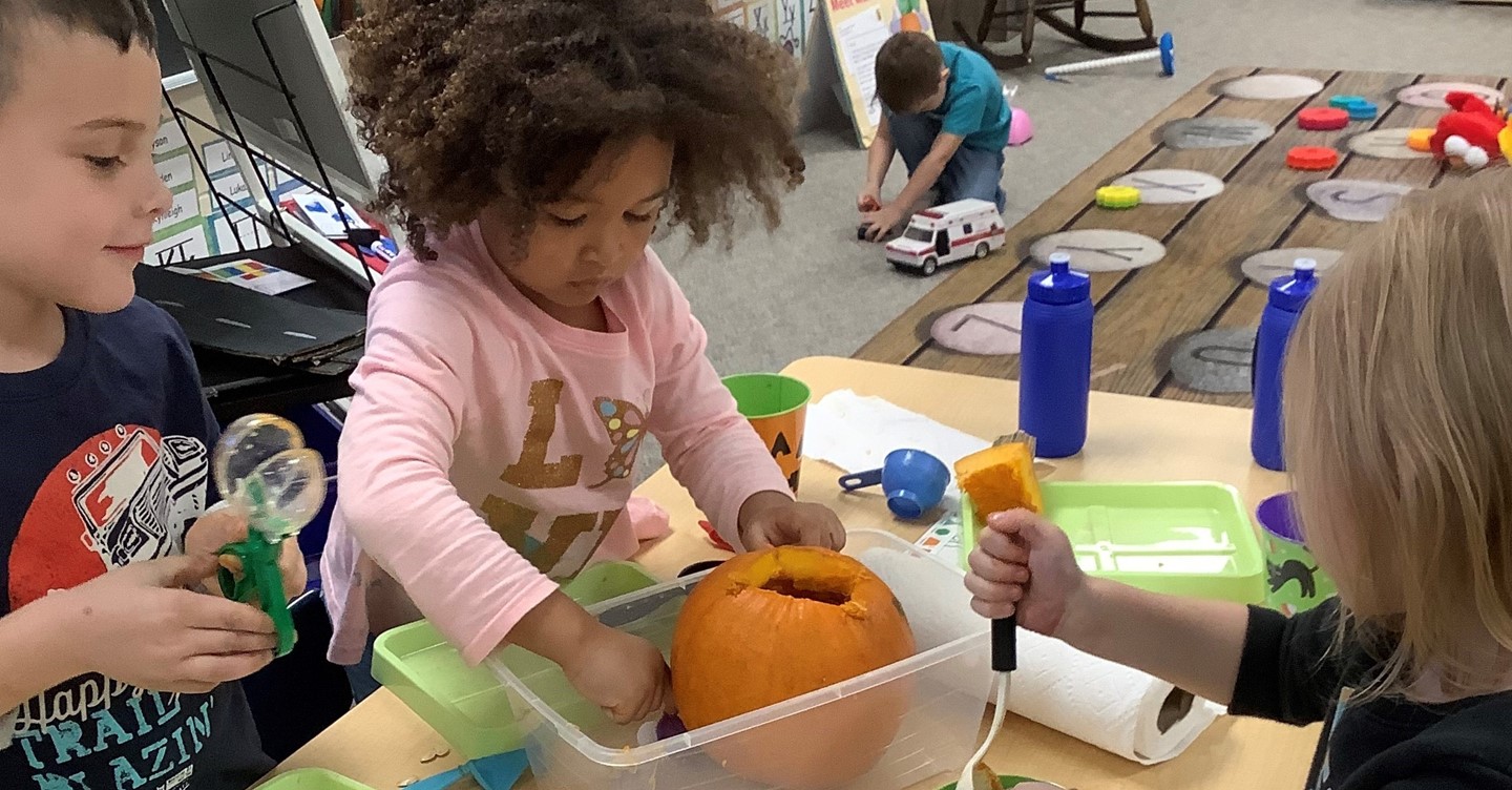 Preschoolers carve pumpkins.